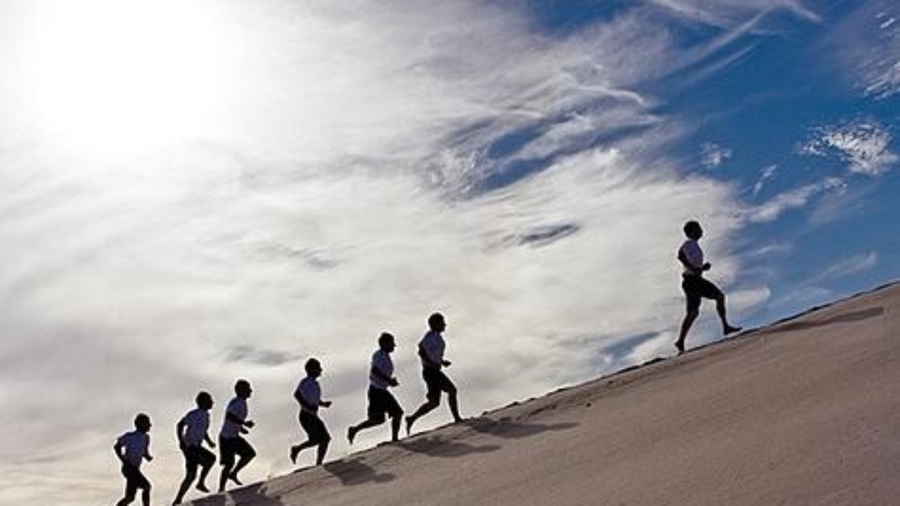 an image of several people running along a beach up hill